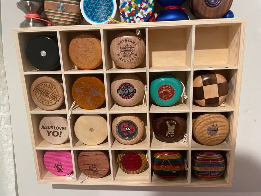 A wall-mounted wooden cubby shelf holding about twenty wooden yo-yos, one per cubby