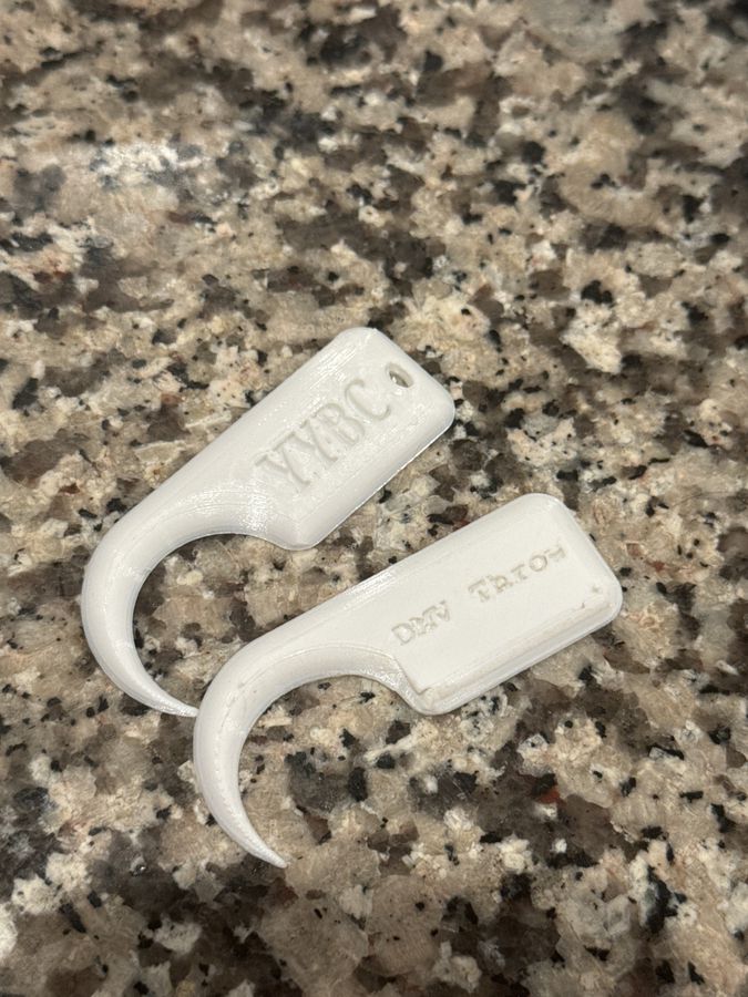 Two white 3D-printed hook-shaped knot picks on a granite counter, one embossed DMV Throw