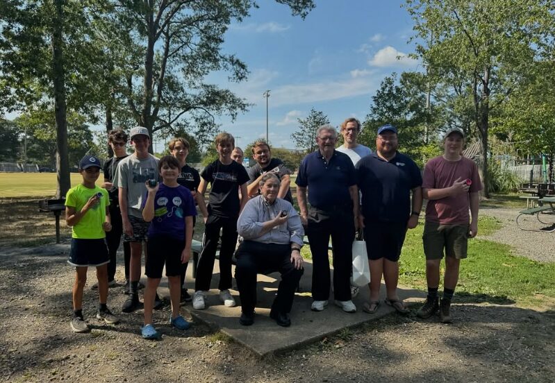About sixteen club members of all ages pose with yo-yos on a shaded path at Quincy Park