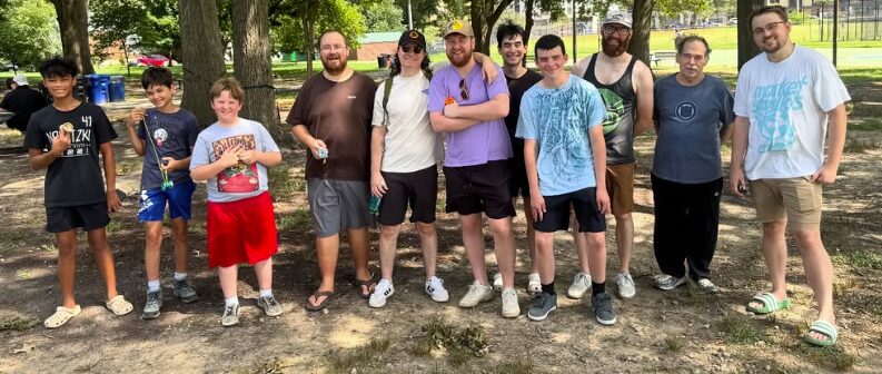 A dozen members, kids and adults, standing together under the trees at Quincy Park