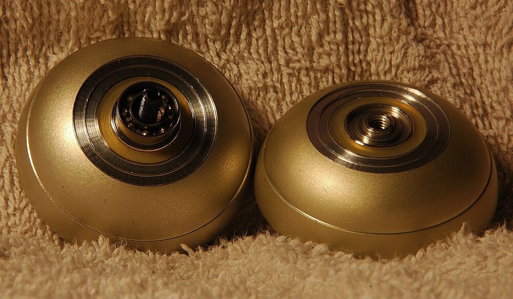 Two gold metal yo-yo halves on carpet, one showing the ball bearing in its hub