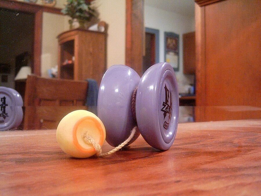 A purple yo-yo on a table with its string tied to a round yellow counterweight