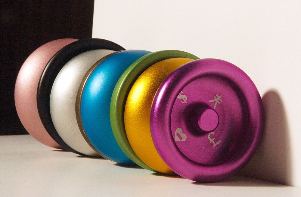A row of anodized aluminum yo-yos in pink, white, black, blue, gold, and purple