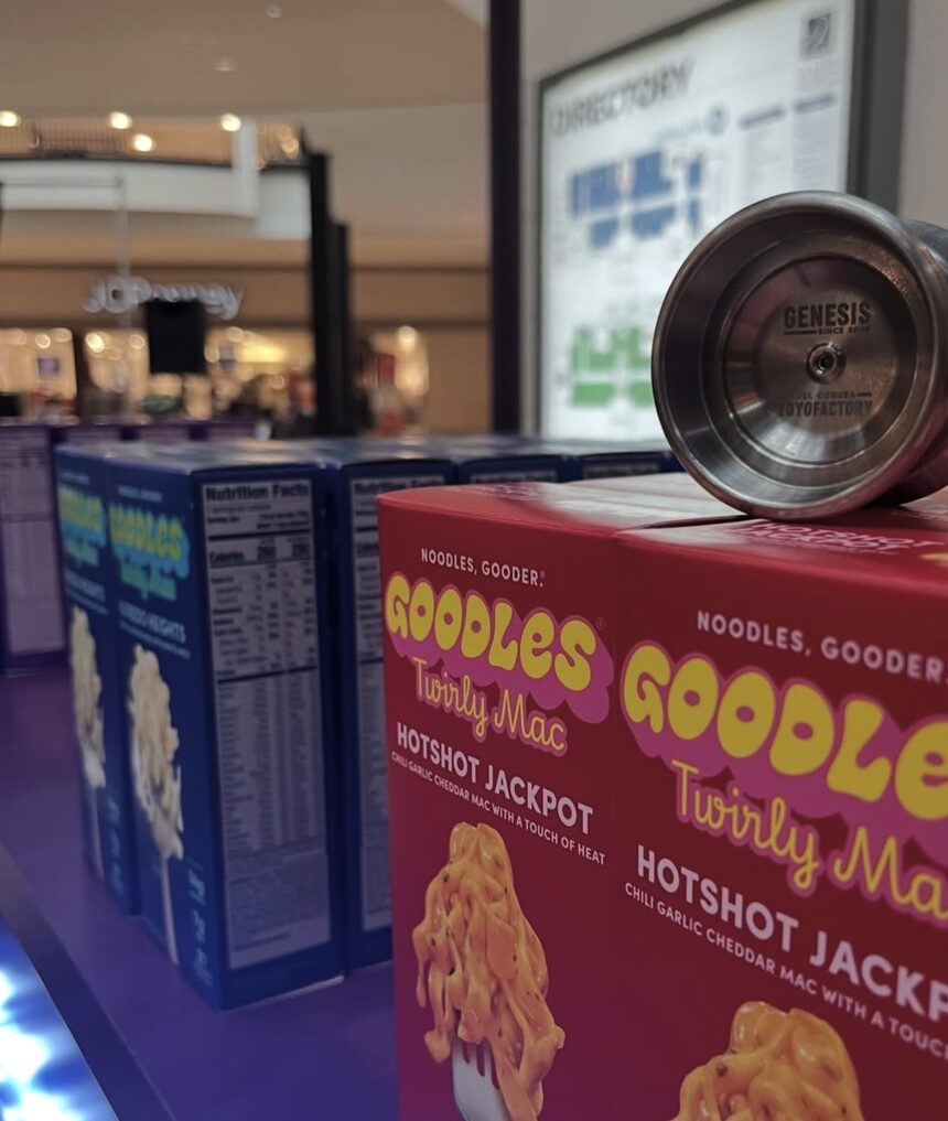 A silver YoYoFactory Genesis yo-yo resting on boxes of Goodles Twirly Mac Hotshot Jackpot at the booth