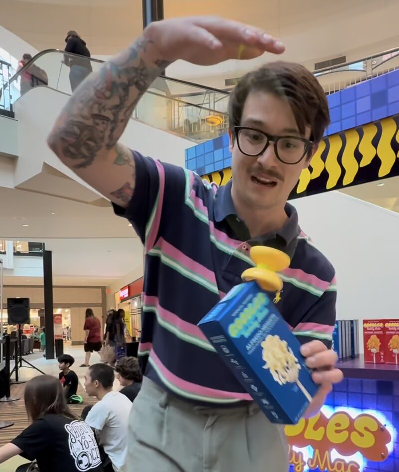 A thrower in a striped polo spins a yellow yo-yo on top of a Twirly Mac box in front of the Goodles booth at Center Court