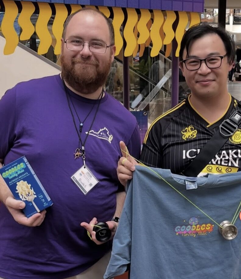 Two throwers smile at the Goodles booth, one holding a box of Twirly Mac and a yo-yo, the other holding up a Goodles Twirly Mac t-shirt and a yo-yo on a string