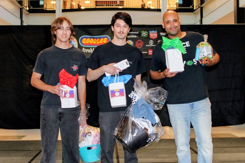 Three competitors on stage holding award bags and prize baskets after their division