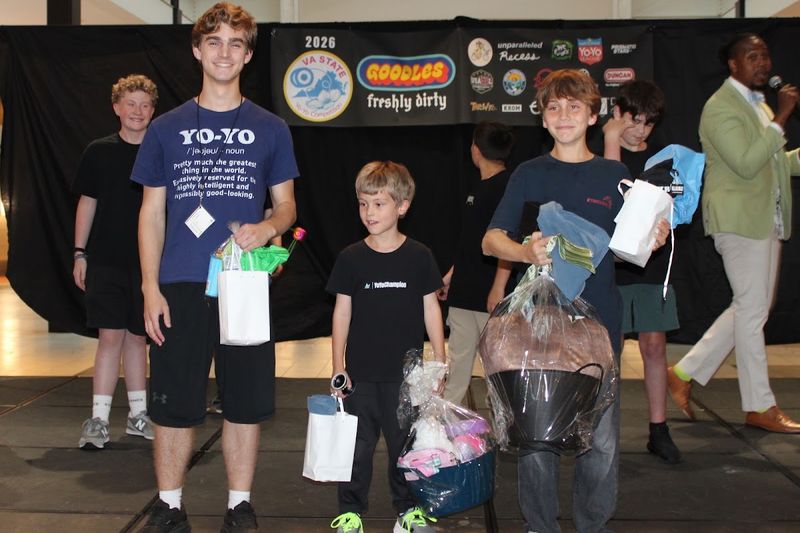 Young Sport, Beginner, and Junior competitors on stage with award bags and prize baskets while the emcee looks on