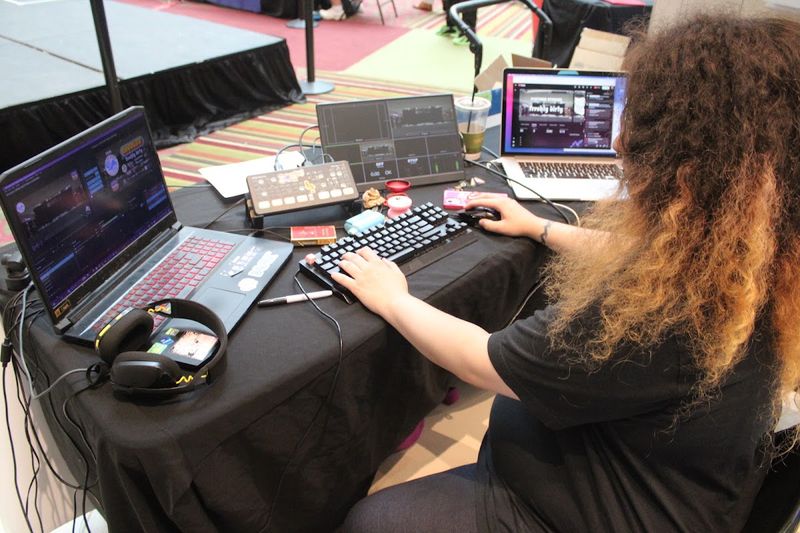 A crew member runs the livestream and music from laptops and a mixer at the side of the stage