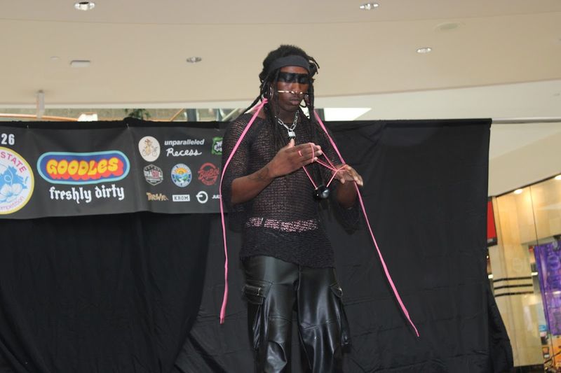 A competitor in sunglasses and a mesh top works pink strings during an offstring routine on stage